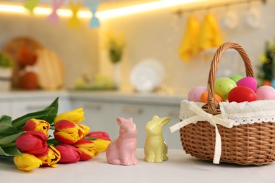 Easter decorations. Wicker basket with painted eggs, tulips and bunny figures on white table indoors, closeup