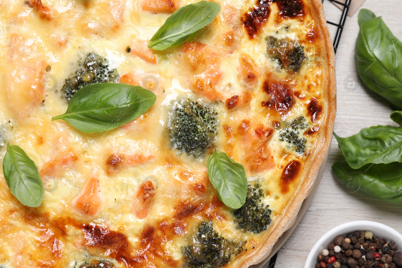 Photo of Delicious homemade quiche with salmon, broccoli and basil leaves on table, flat lay