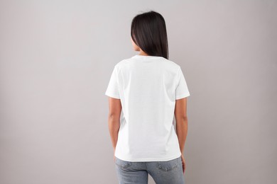 Woman wearing white t-shirt on light grey background, back view