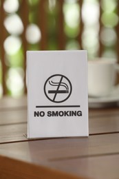 Photo of No Smoking sign on wooden table against blurred background, closeup