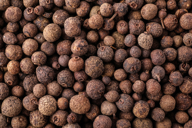 Black pepper grains as background, top view