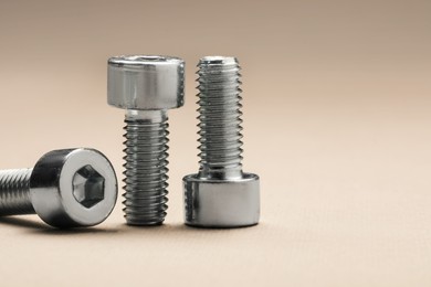 Photo of Metal socket screws on beige background, closeup. Space for text