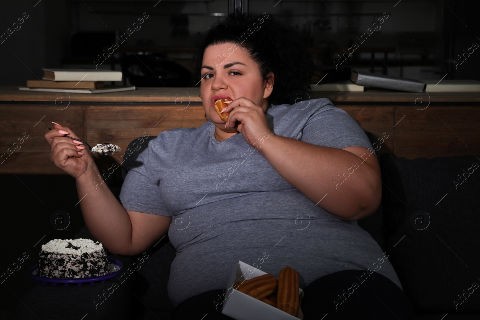 Photo of Depressed overweight woman eating sweets in living room at night