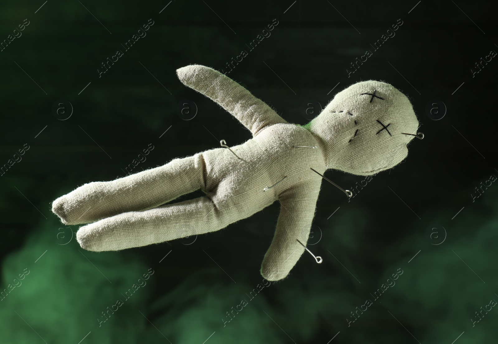 Photo of Voodoo doll with pins and smoke on dark green background