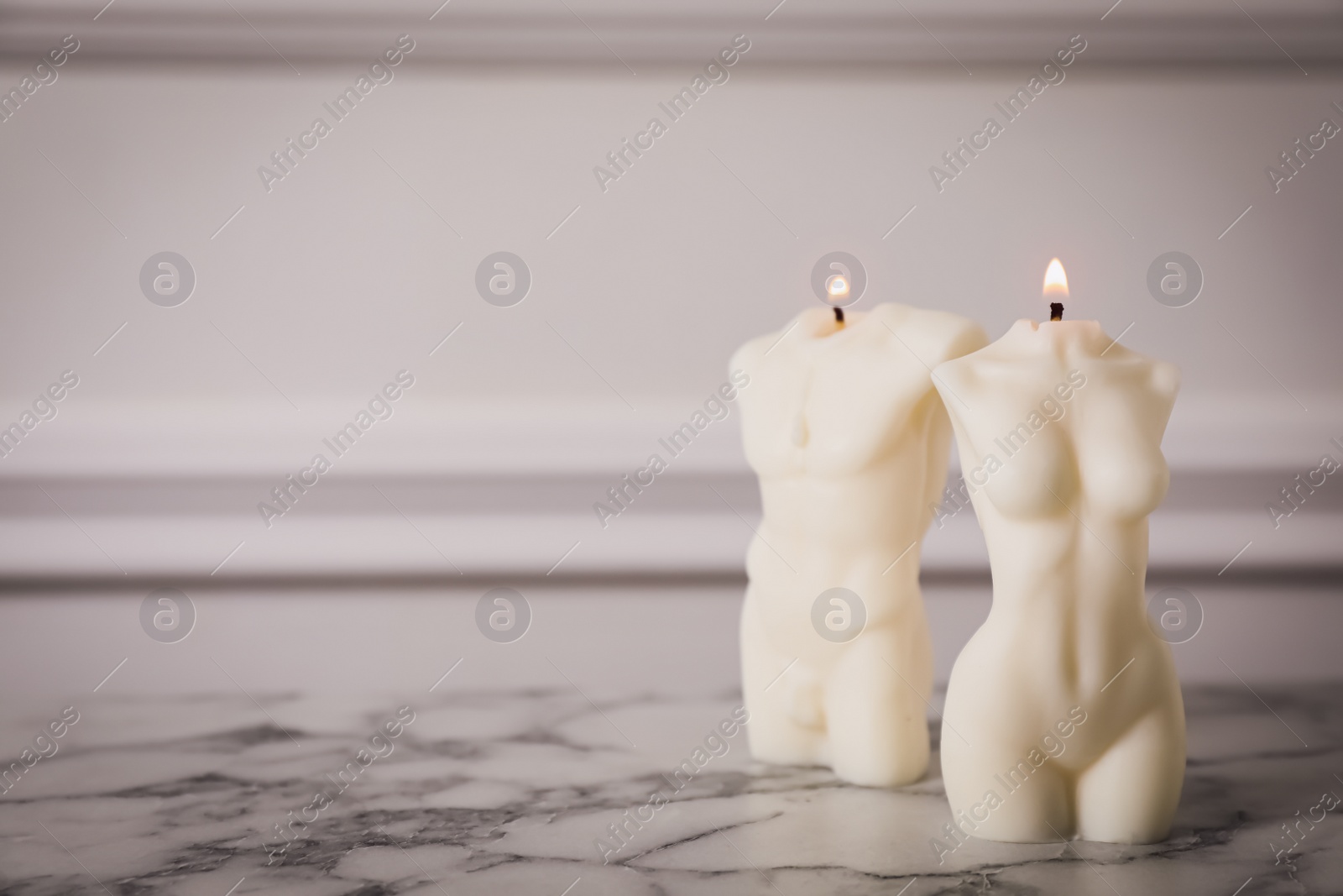 Photo of Stylish female and male body shaped candles on white marble table. Space for text