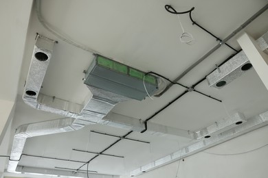 Photo of Ventilation system and wires on white ceiling indoors