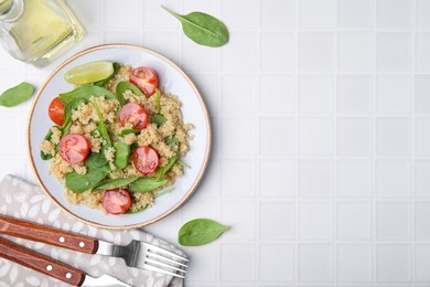Delicious quinoa salad with tomatoes and spinach leaves served on white tiled table, flat lay. Space for text
