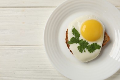 Photo of Plate with tasty fried egg and slice of bread on white wooden table, top view. Space for text