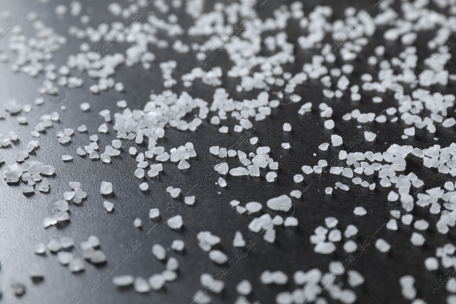 Photo of Scattered white natural salt on black table, closeup