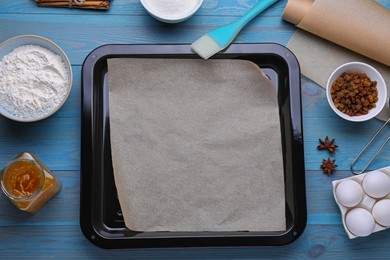 Baking pan with parchment paper, different ingredients and kitchen tools on light blue wooden table, flat lay