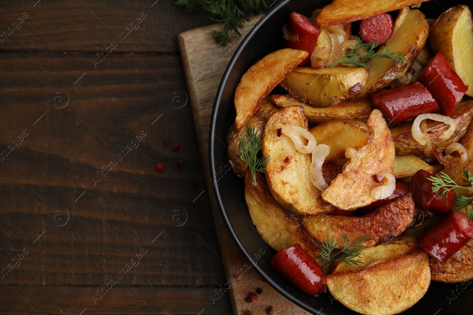 Photo of Delicious baked potato with thin dry smoked sausages, onion and dill in bowl on wooden table, top view. Space for text