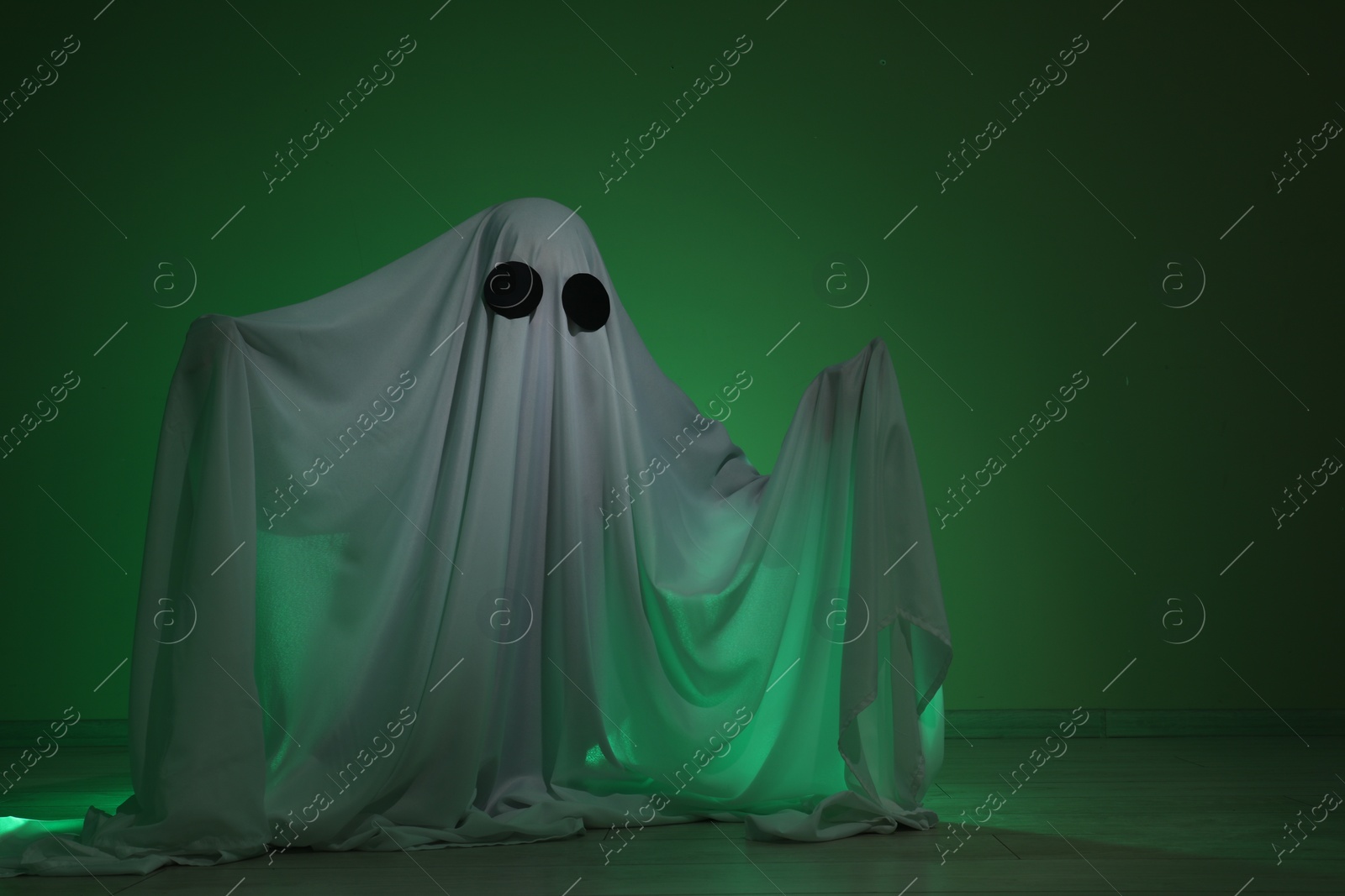 Photo of Creepy ghost. Woman covered with sheet in green light, space for text