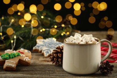 Delicious hot chocolate with marshmallows and Christmas decor on wooden table against blurred lights, space for text