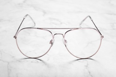 Photo of Glasses in stylish frame on white marble table, closeup