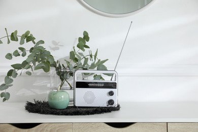 Beautiful eucalyptus branches in vase and radio receiver on table indoors, space for text