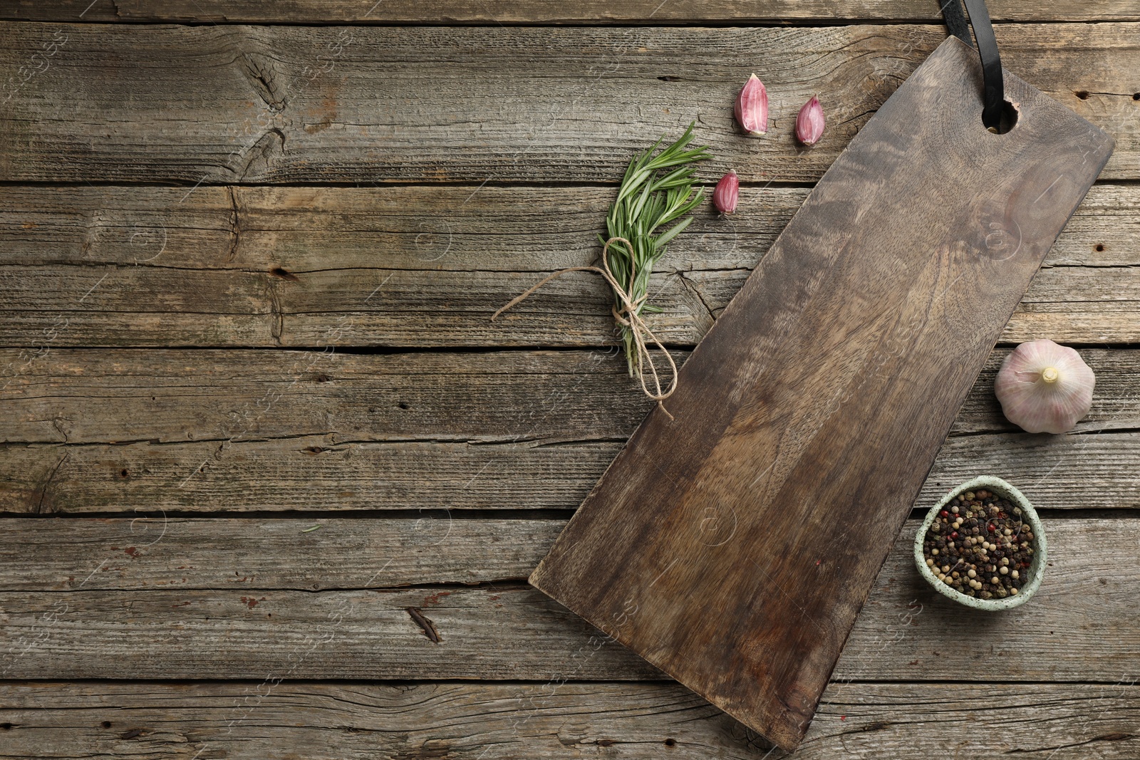 Photo of Cutting board, garlic, pepper and rosemary on wooden table, flat lay. Space for text