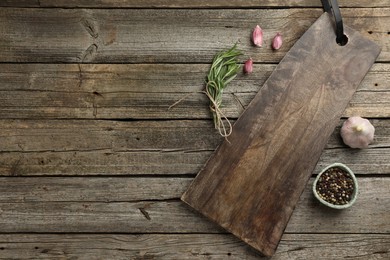 Photo of Cutting board, garlic, pepper and rosemary on wooden table, flat lay. Space for text