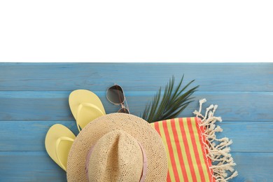 Photo of Light blue wooden surface with beach towel, straw hat, flip flops and sunglasses on white background, top view