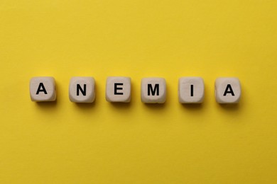 Photo of Word Anemia made with wooden cubes on yellow background, flat lay