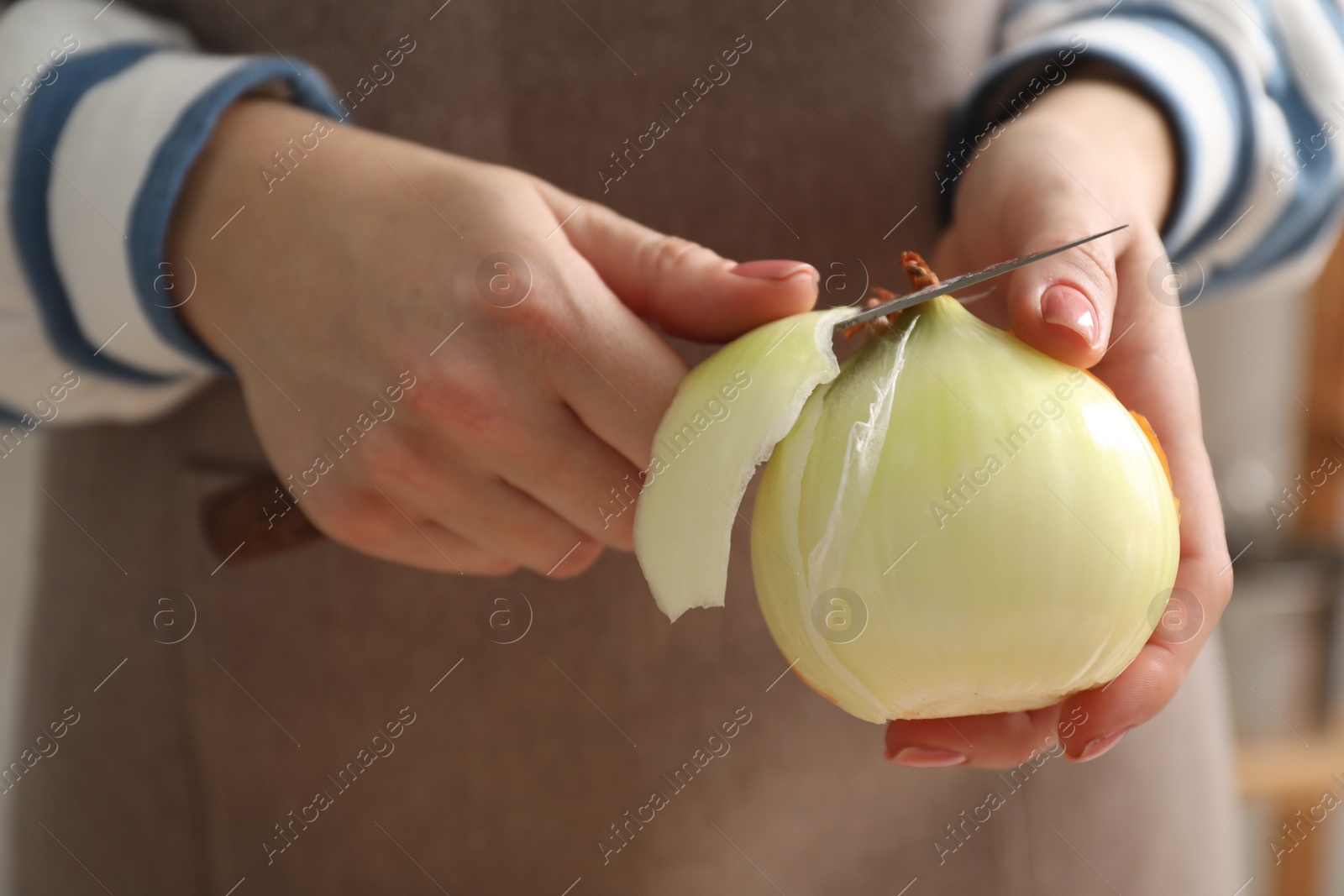 Photo of Woman peeling fresh onion with knife indoors, closeup