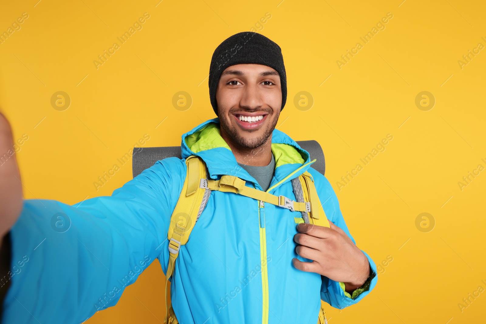 Photo of Happy tourist with backpack taking selfie on yellow background