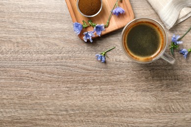Photo of Glass cup of delicious chicory drink, powder and flowers on wooden table, flat lay. Space for text