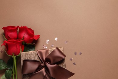 Photo of Beautiful gift box, flowers and confetti on brown background, flat lay. Space for text