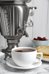 Photo of Metal samovar and cup of tea on white marble table