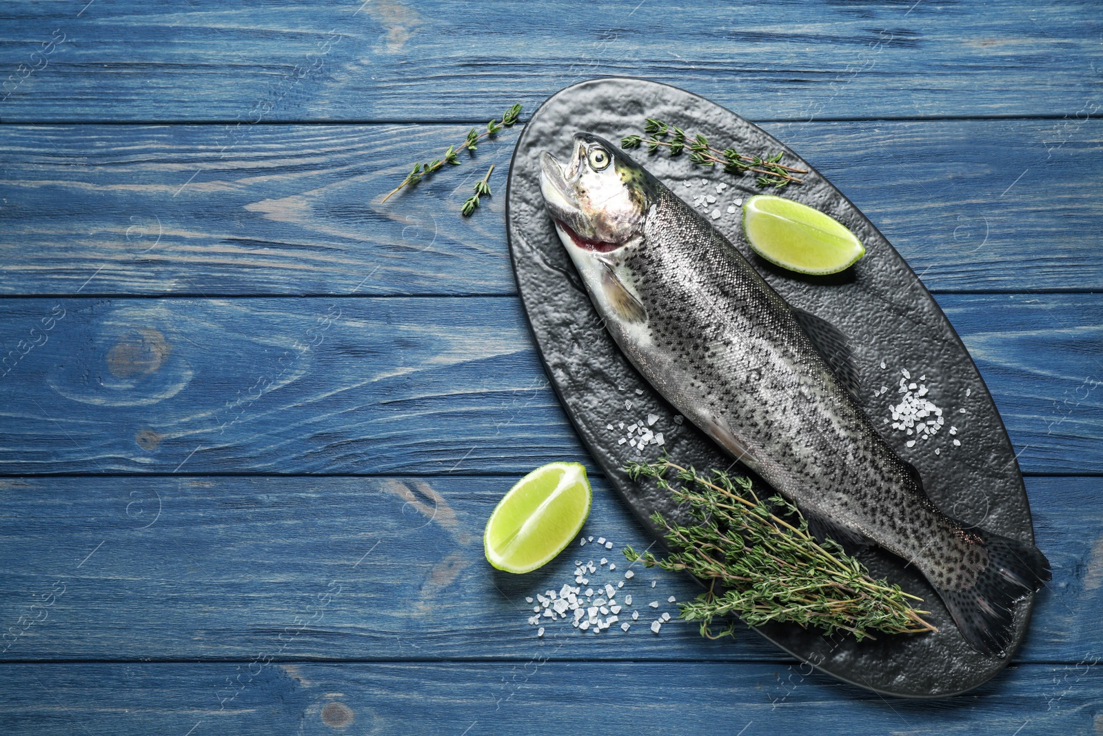 Photo of Raw cutthroat trout fish on blue wooden table, flat lay. Space for text