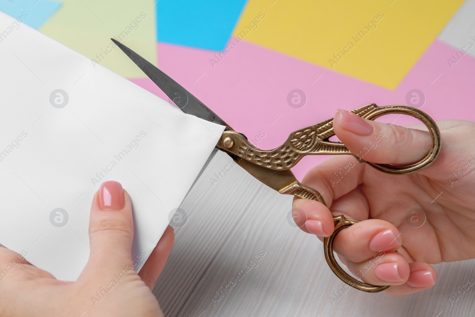 Photo of Woman cutting paper with scissors at white wooden table, closeup