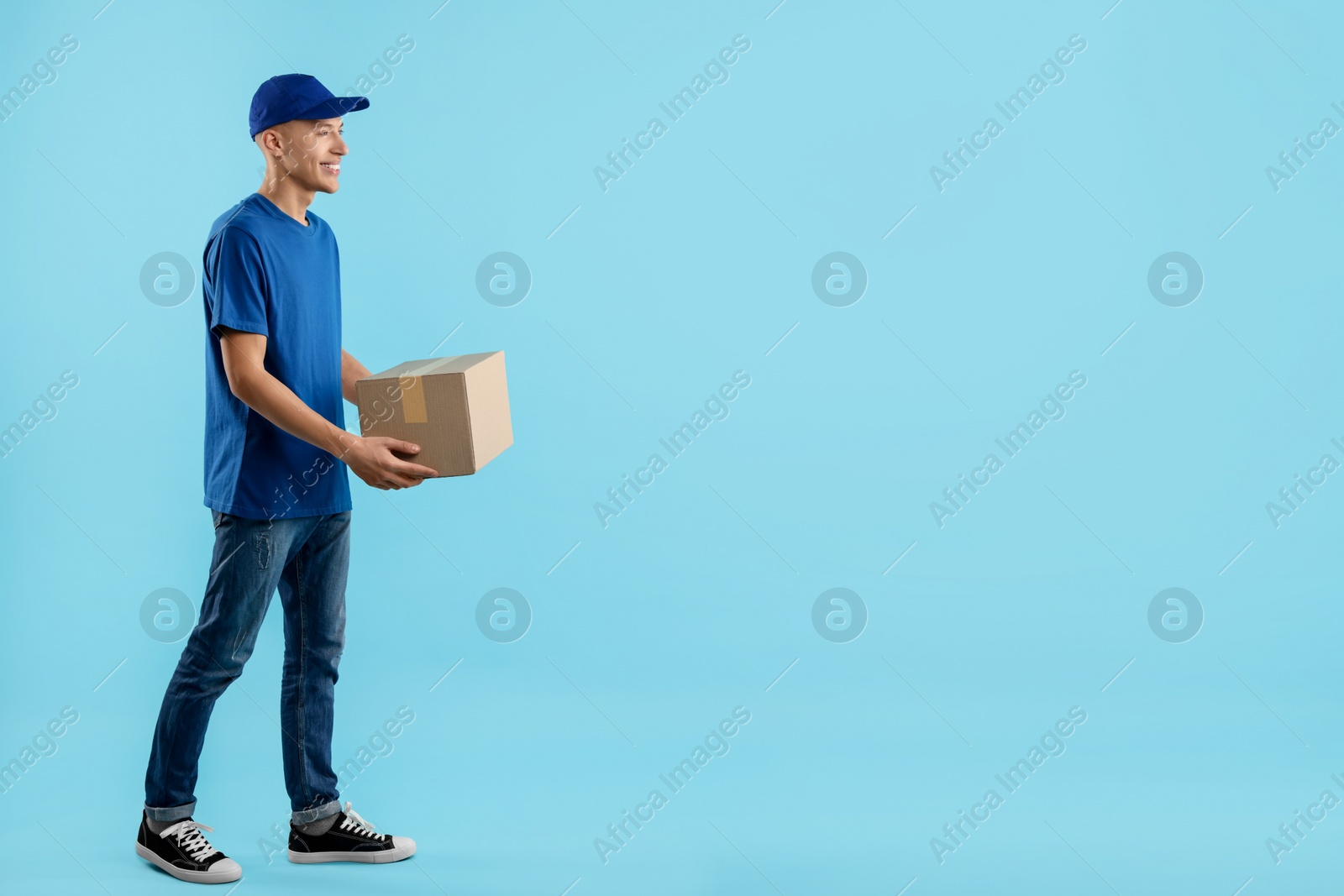 Photo of Happy courier with parcel on light blue background. Space for text