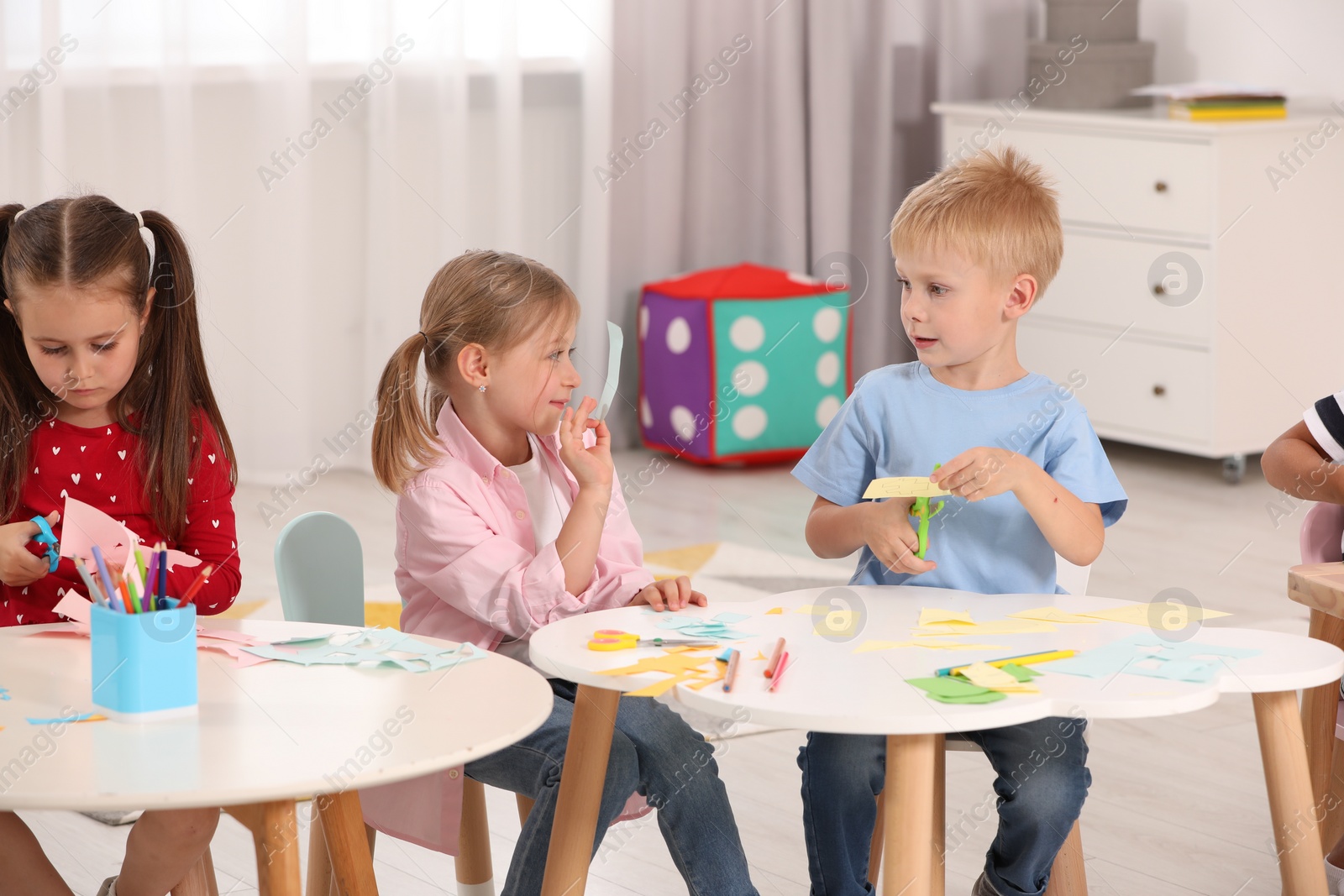 Photo of Group of cute little children making toys from color paper at desks in kindergarten. Playtime activities