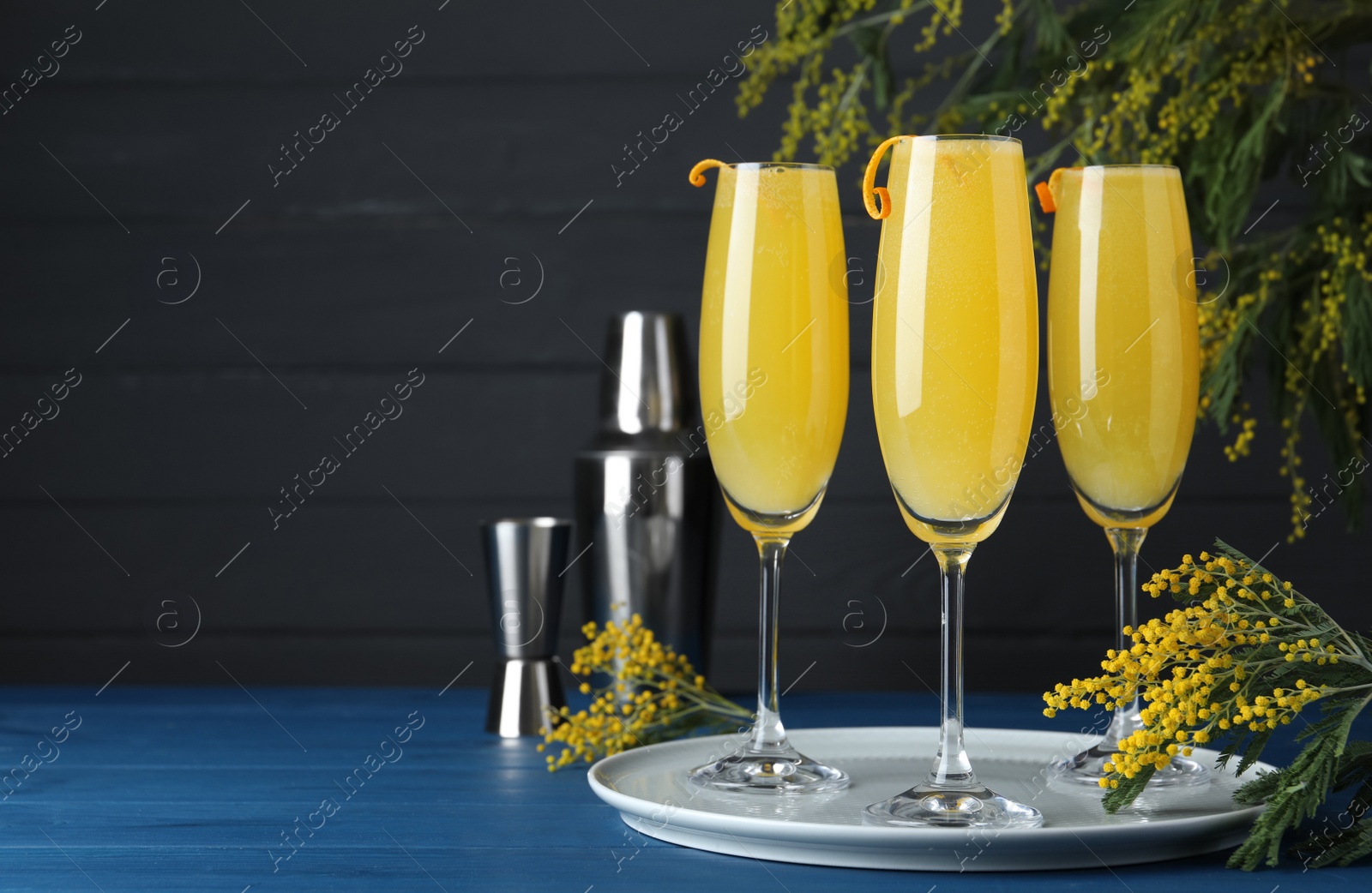 Photo of Glasses of Mimosa cocktail with flowering branches on light blue wooden table. Space for text