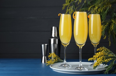 Photo of Glasses of Mimosa cocktail with flowering branches on light blue wooden table. Space for text