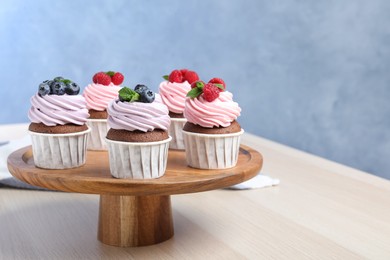 Photo of Wooden dessert stand with sweet cupcakes on light table. Space for text