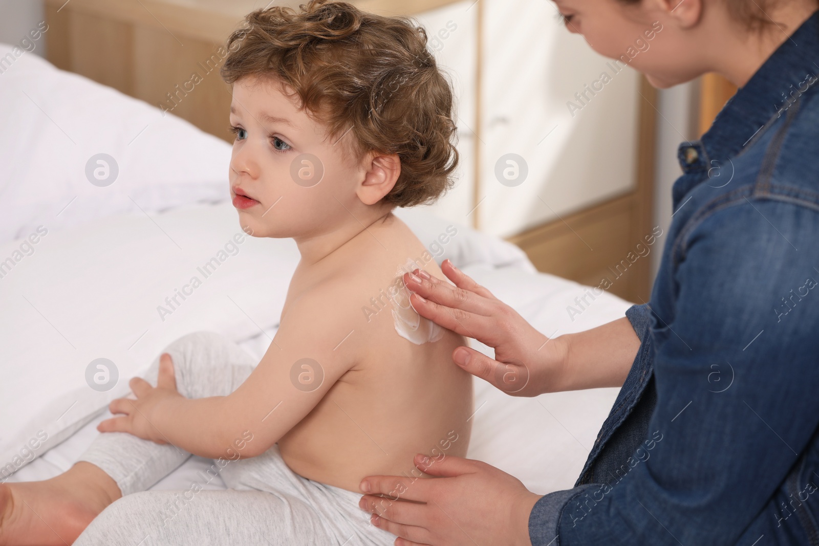 Photo of Mother applying ointment onto her son`s back on bed indoors