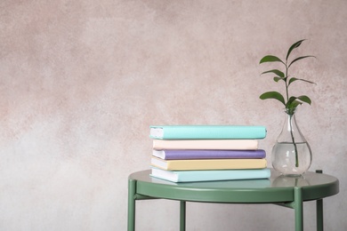 Photo of Stack of books and vase on table against color background. Space for text