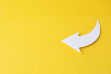Photo of White curved paper arrow on yellow background, top view. Space for text