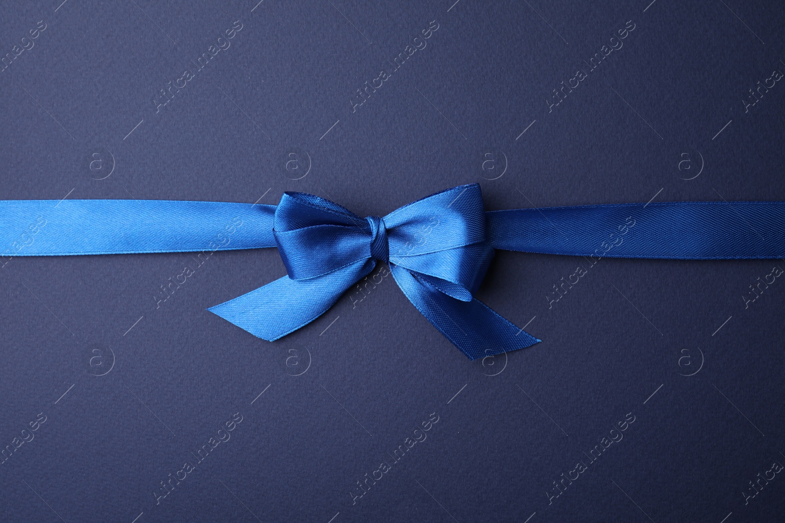 Photo of Bright satin ribbon with bow on blue background, top view