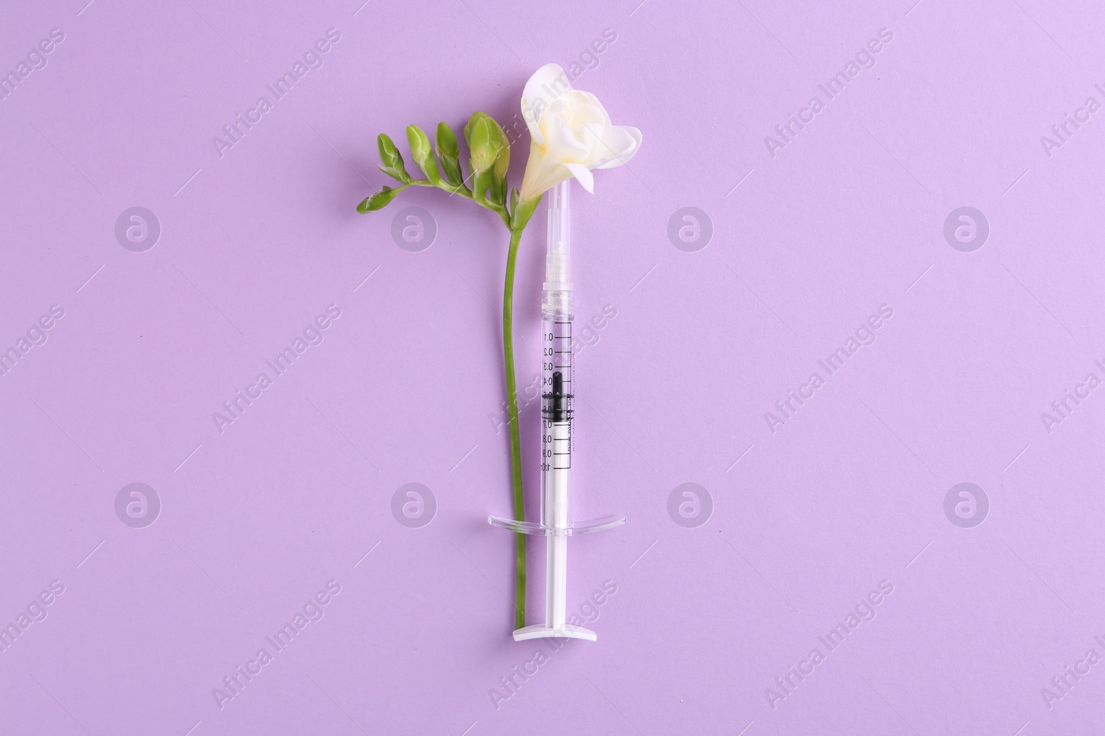 Photo of Cosmetology. Medical syringe and freesia flower on violet background, top view