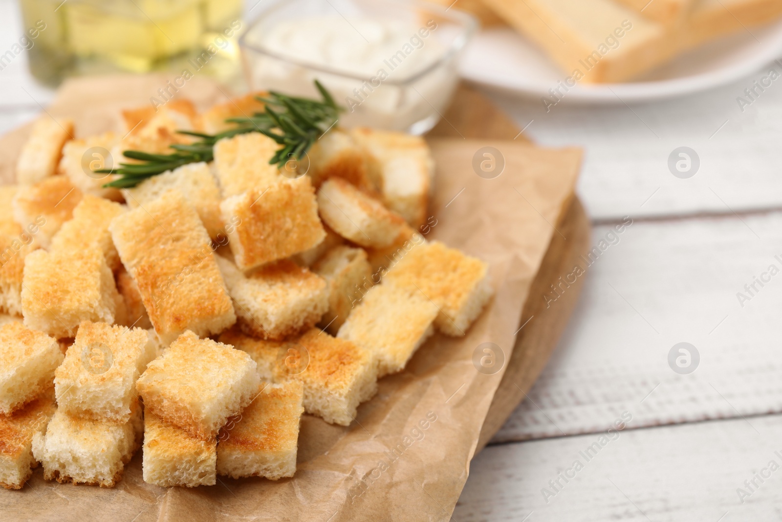 Photo of Delicious crispy croutons with rosemary on white wooden table, closeup
