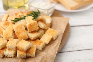 Photo of Delicious crispy croutons with rosemary on white wooden table, closeup