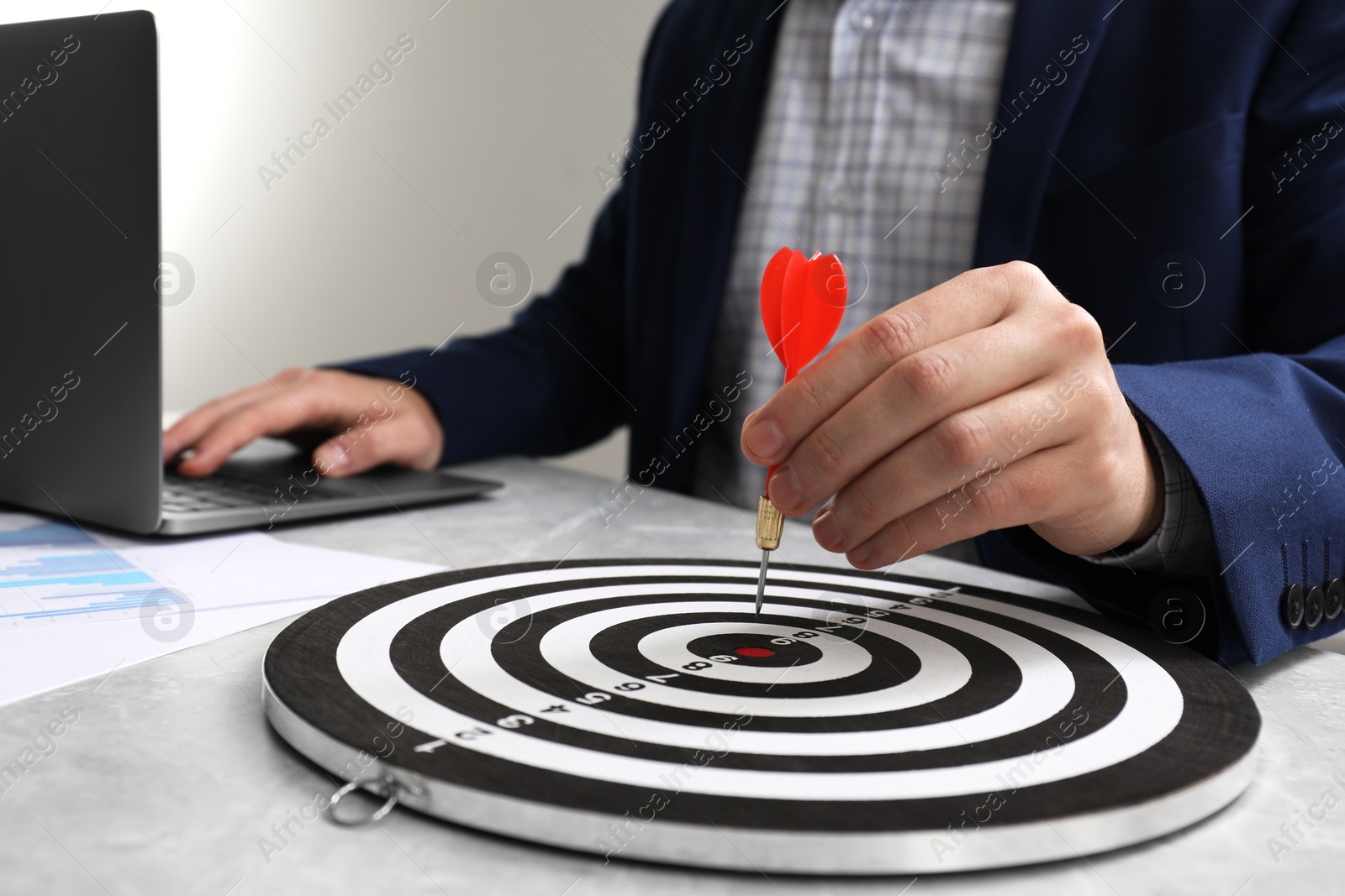 Photo of Business targeting concept. Man with dart aiming at dartboard at table indoors, closeup