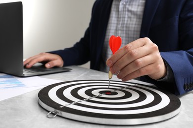 Business targeting concept. Man with dart aiming at dartboard at table indoors, closeup