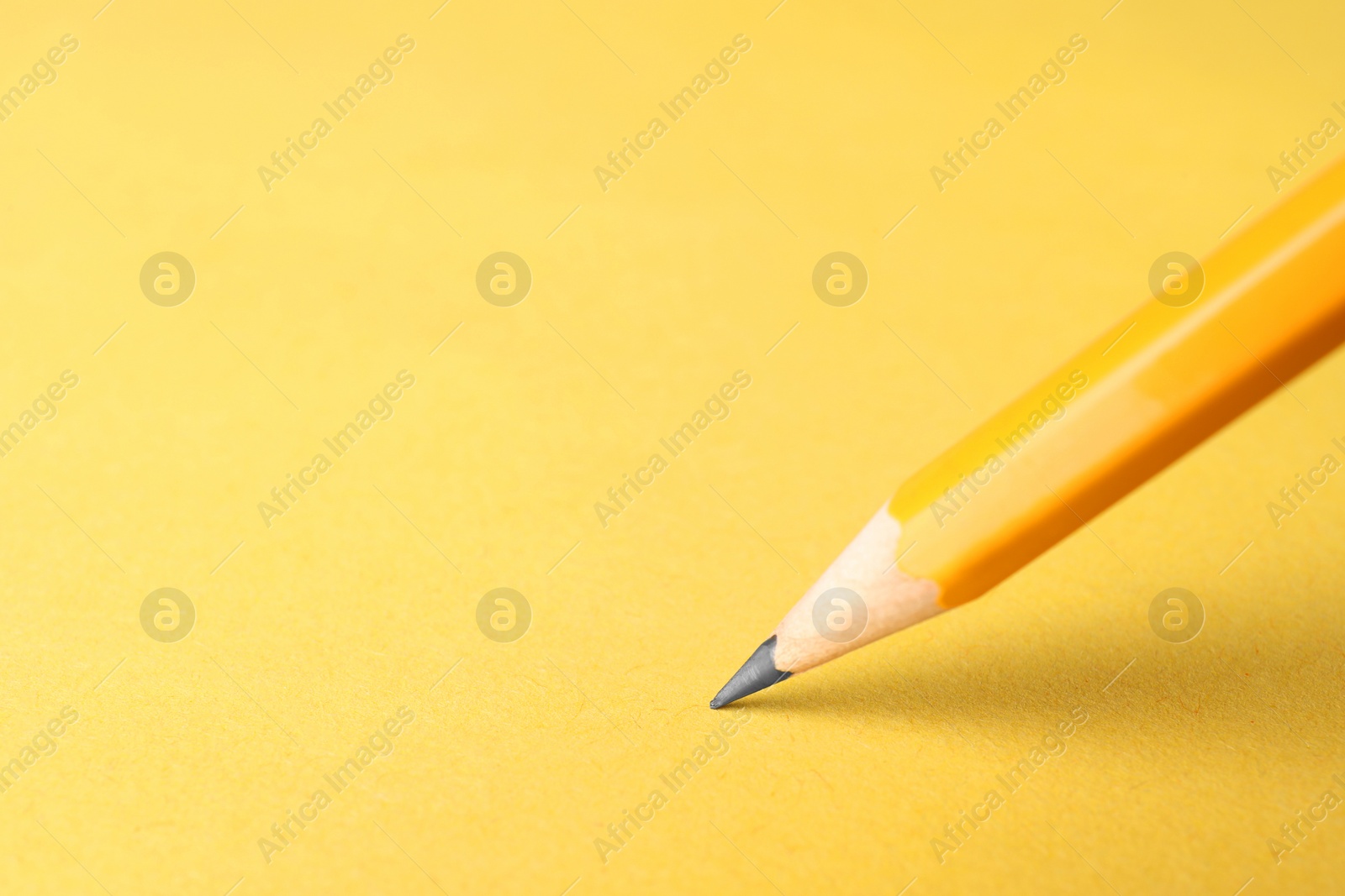 Photo of One sharp graphite pencil on yellow background, closeup. Space for text