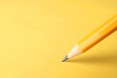 Photo of One sharp graphite pencil on yellow background, closeup. Space for text