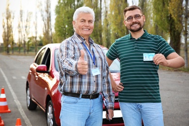Photo of Senior instructor and happy man with driving license outdoors