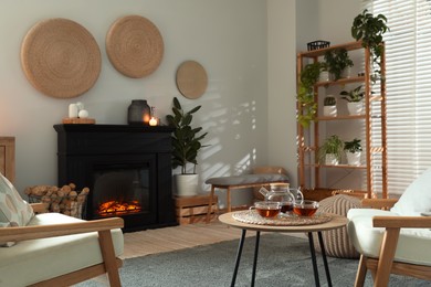 Stylish fireplace near coffee table with tea in cosy living room. Interior design