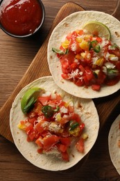 Photo of Delicious tacos with vegetables, lime and ketchup on wooden table, flat lay