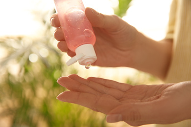 Photo of Young woman applying antiseptic gel outdoors, closeup